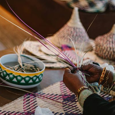 Emirati woman is weaving traditional basket from palm leaves. Emirati woman with mask on the face weaving traditional basket from palm leaves